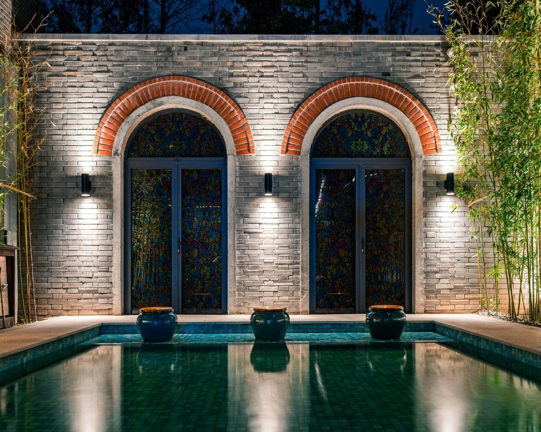 Abendlich beleuchteter Spa-Pool vor Bogenfassade mit Bambus